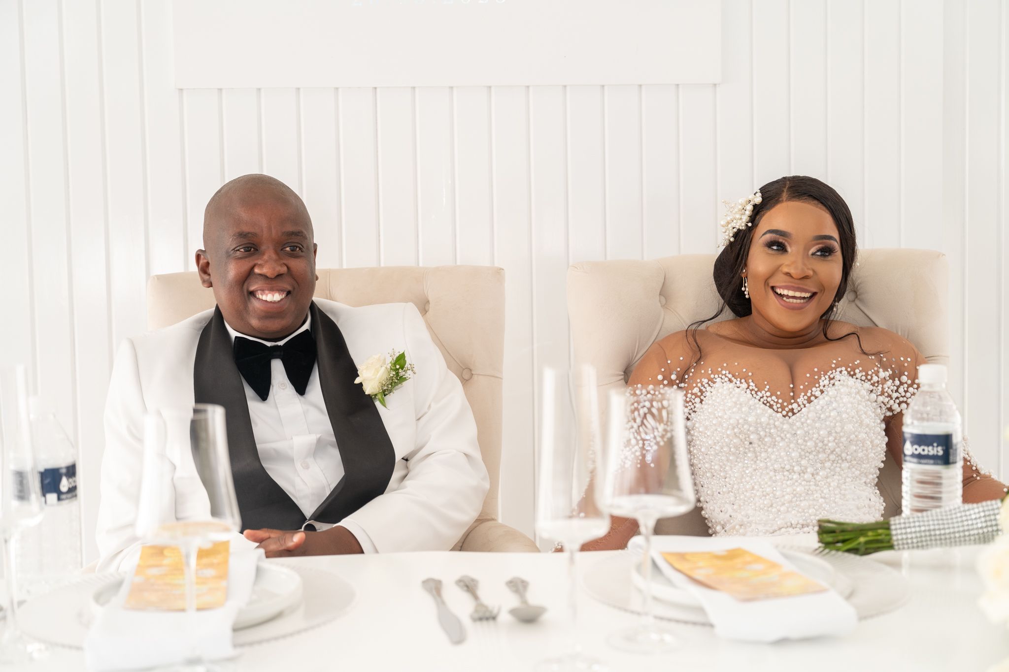 Wedding couple in formal attire sharing a candid moment at their reception table.