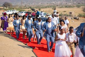Wedding party members walking down a red carpet aisle outdoors with mountains and desert scenery.