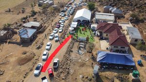 Drone shot of outdoor wedding venue with red carpet and parked cars in arid landscape.