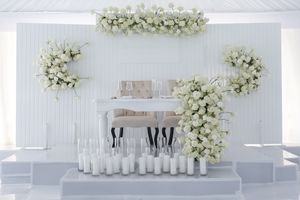 Wedding venue backdrop decorated with white floral arrangements and glass vases.