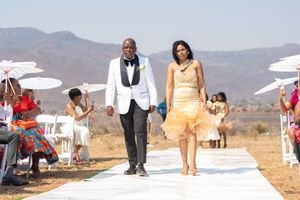 Wedding couple walking down white aisle runner with mountain landscape in background.