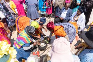 Group gathered around traditional cooking setup with colorful clothing and head wraps.