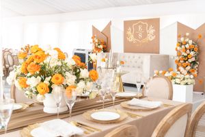 Elegant wedding reception table setting with orange and white floral centerpieces and gold accents.