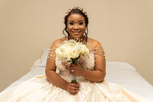 Bride in off-shoulder white ball gown holds bouquet of white flowers.