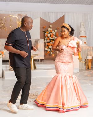 Couple dancing in formal attire with peach mermaid dress and black outfit at decorated venue.