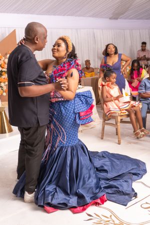 Couple dancing at celebration event with guests seated in background.