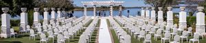 Elegant outdoor wedding ceremony setup with white chairs lined up along an aisle leading to a covered altar.
