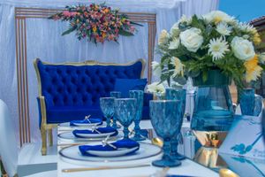 Elegant table setting with blue glasses, white flowers and tufted royal blue velvet chair.