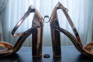 Wedding rings positioned between elegant black high heels against a light background.