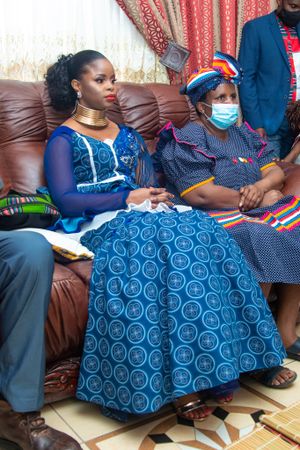 Two people seated on brown leather couch wearing traditional African attire.