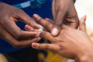 Close up of hands exchanging an engagement ring with manicured nails.