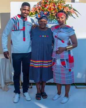 Family wearing coordinated African-inspired outfits posing with floral arrangement.