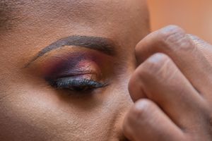 Close-up of vibrant purple and pink eye makeup being applied with artistic precision.