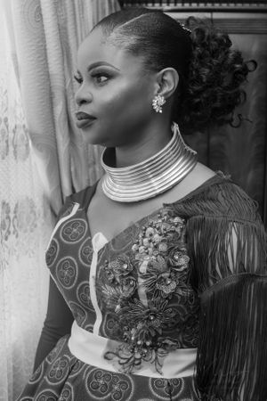 Black and white portrait showcasing traditional African-inspired fashion with ornate neckpiece and patterned dress.
