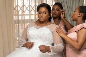 Wedding preparation scene with bride in white gown getting final adjustments.