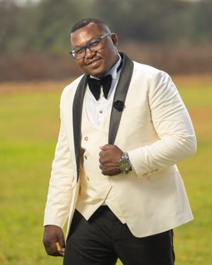 Groom in a stylish white tuxedo jacket and black bow tie poses confidently outdoors.