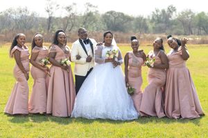 Wedding party in coordinated pink and black attire poses together on a grassy field.