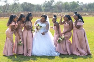 Wedding party with bridesmaids in pink dresses gathering joyfully on a grassy field.