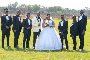 Wedding party with groomsmen in black suits gathered on a green field.