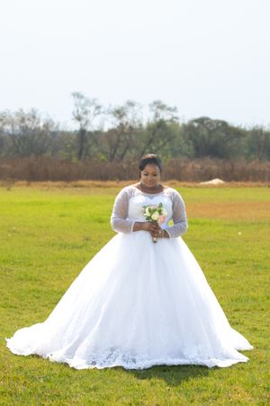 Bride in a beautiful white lace ball gown holds a bouquet while standing in a field.