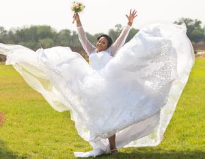 Joyful bride in flowing white dress twirls with excitement in an outdoor field.