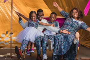 Family group in coordinated African print outfits dancing and celebrating under a tent.