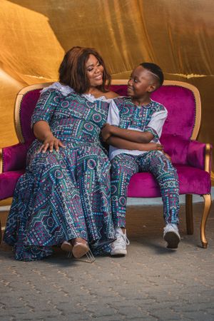 A mother and child share a joyful moment on a purple velvet sofa while wearing matching blue patterned outfits.