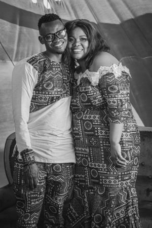 A couple wearing matching traditional African print outfits pose together at an event.