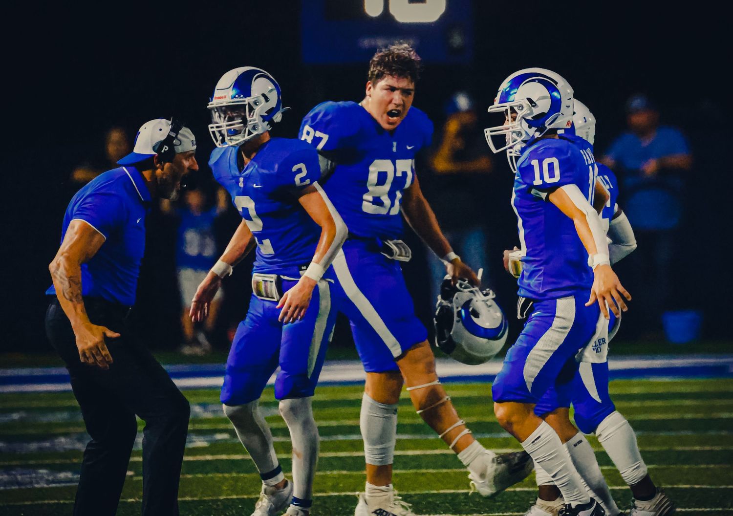High school football players in blue uniforms gather on the sideline during a game.