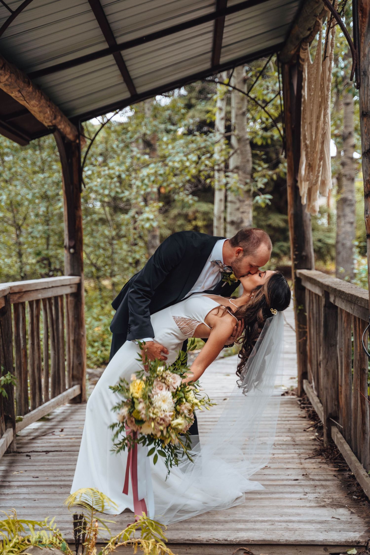 The groom dips his bride in a kiss on a rustic wooden bridge. Banff wedding.