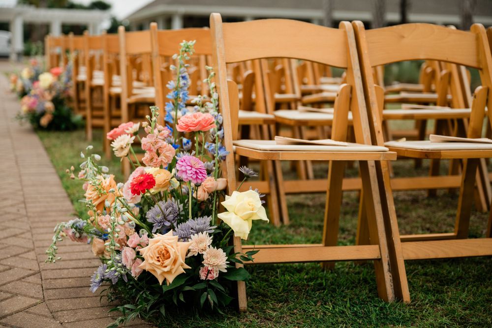 Wooden folding chairs lined up with colorful floral arrangements for an outdoor wedding ceremony.