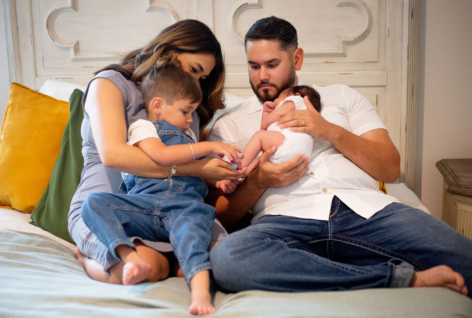 A family spends quality time together on a bed with a yellow pillow, bonding with their new baby.