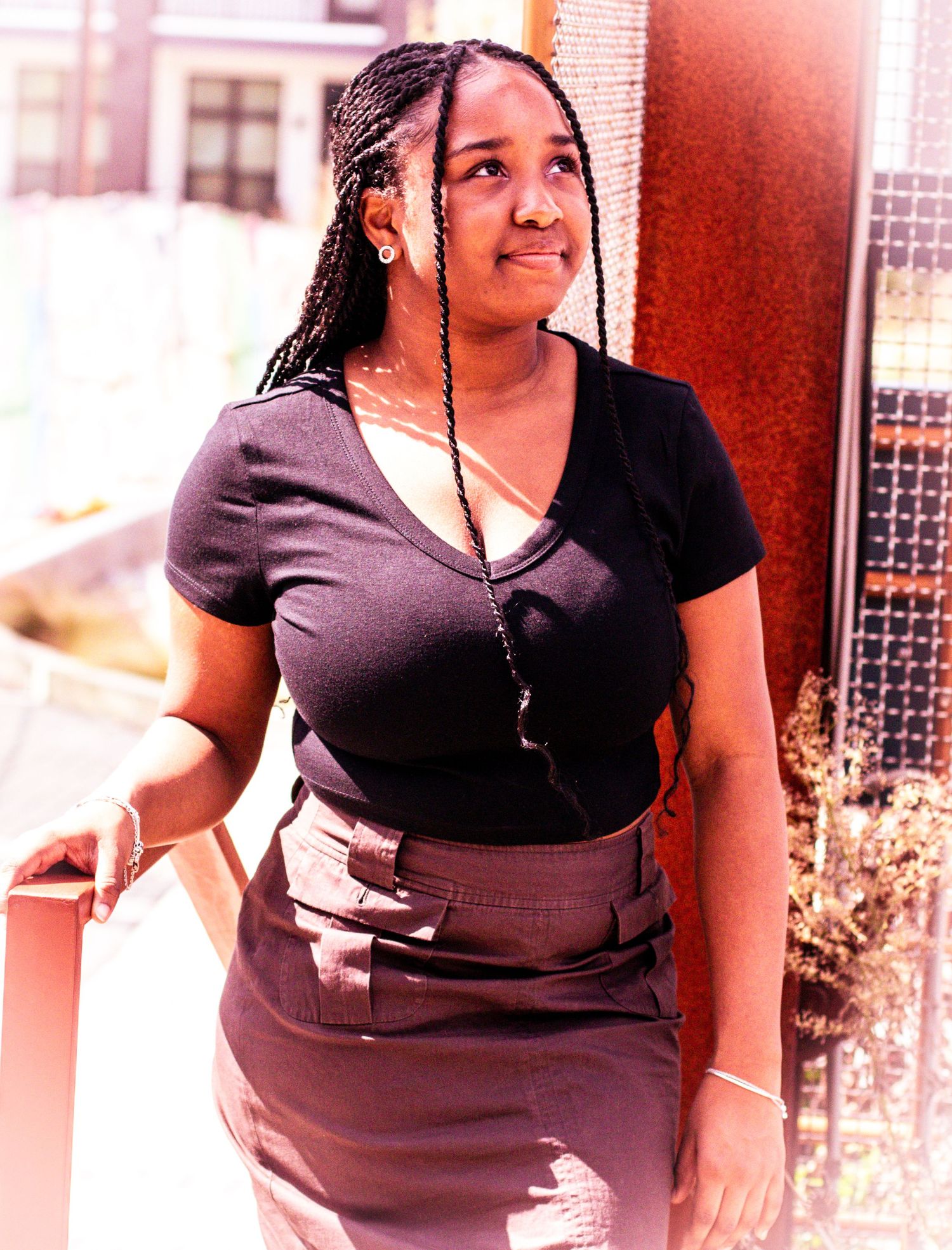 Portrait of a person in black attire with braided hair in an outdoor urban setting.