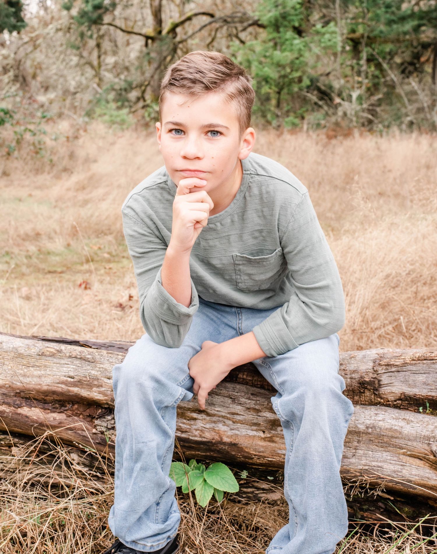 Portrait of young person sitting on log in natural outdoor setting.