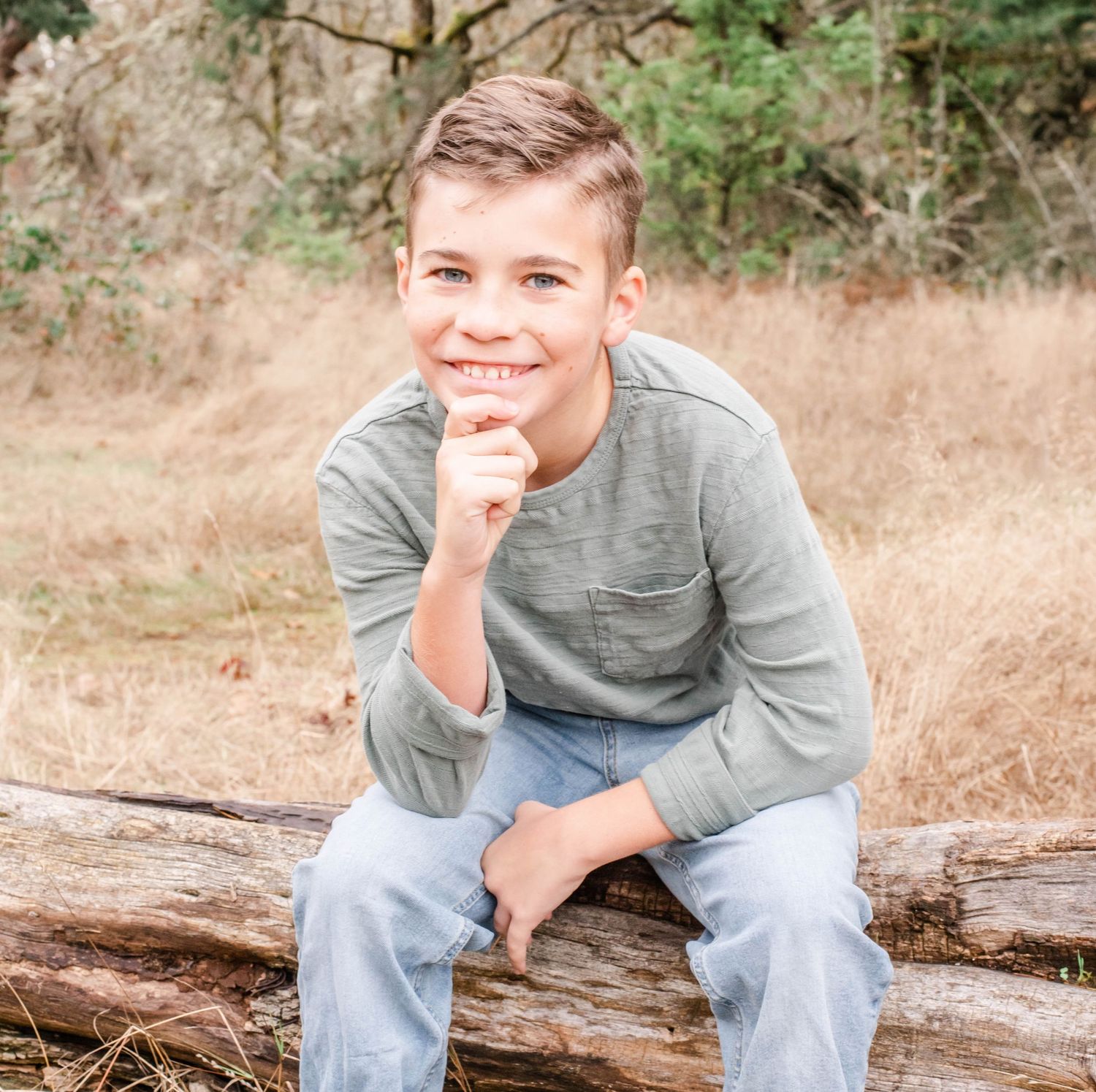 Youth sitting on fallen log in outdoor setting with autumn colors.