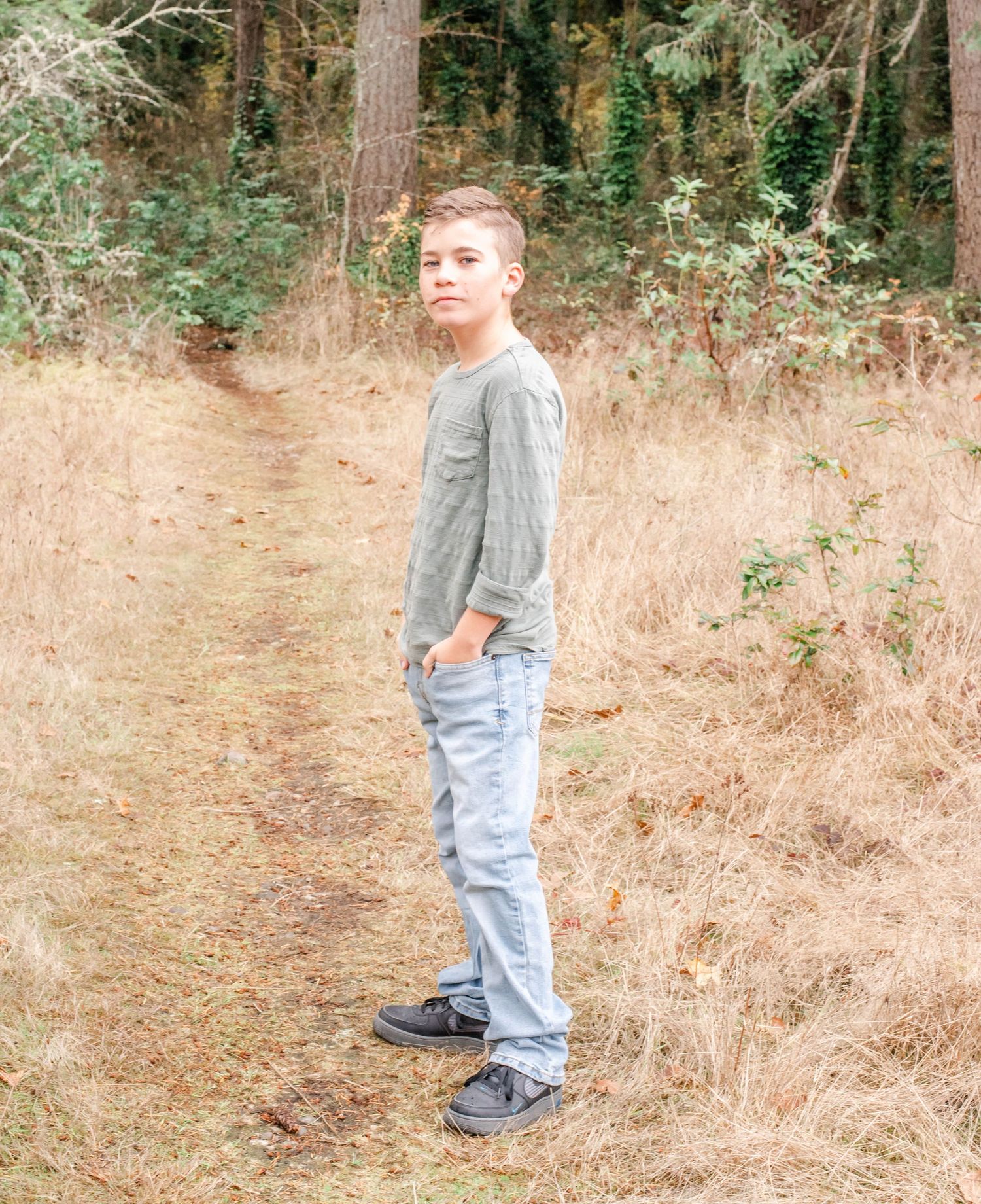 Full length portrait of youth standing in wooded area with brown grass.