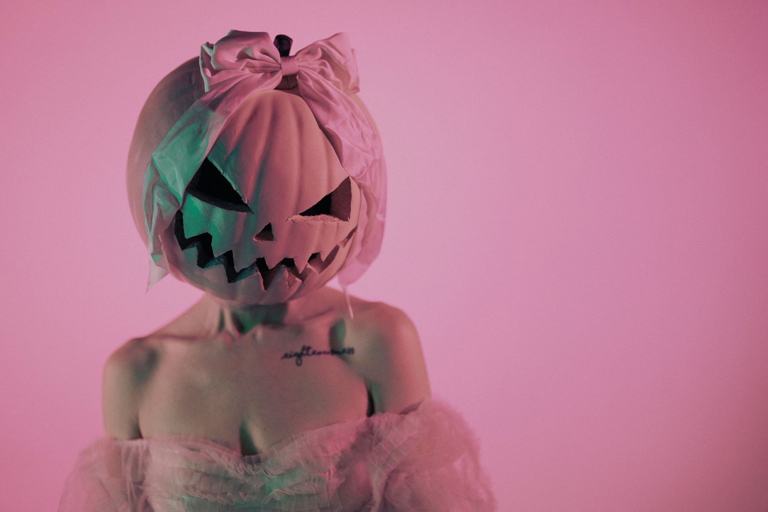 Halloween-themed portrait with pumpkin mask against pink background.