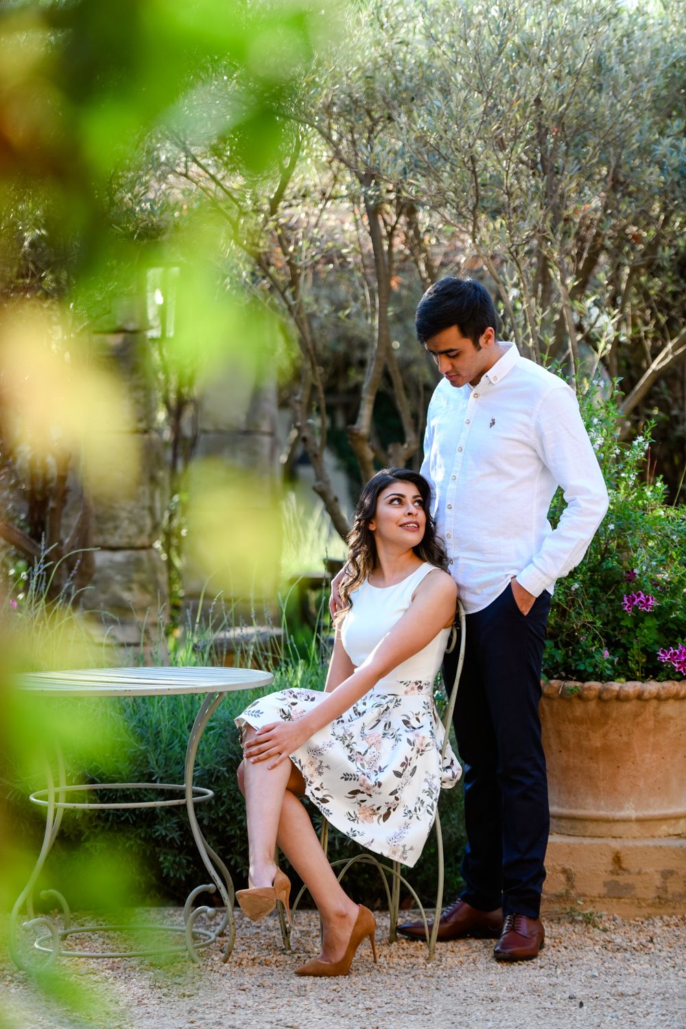 Couple portrait in a garden venue, with the woman seated on a low stone wall.