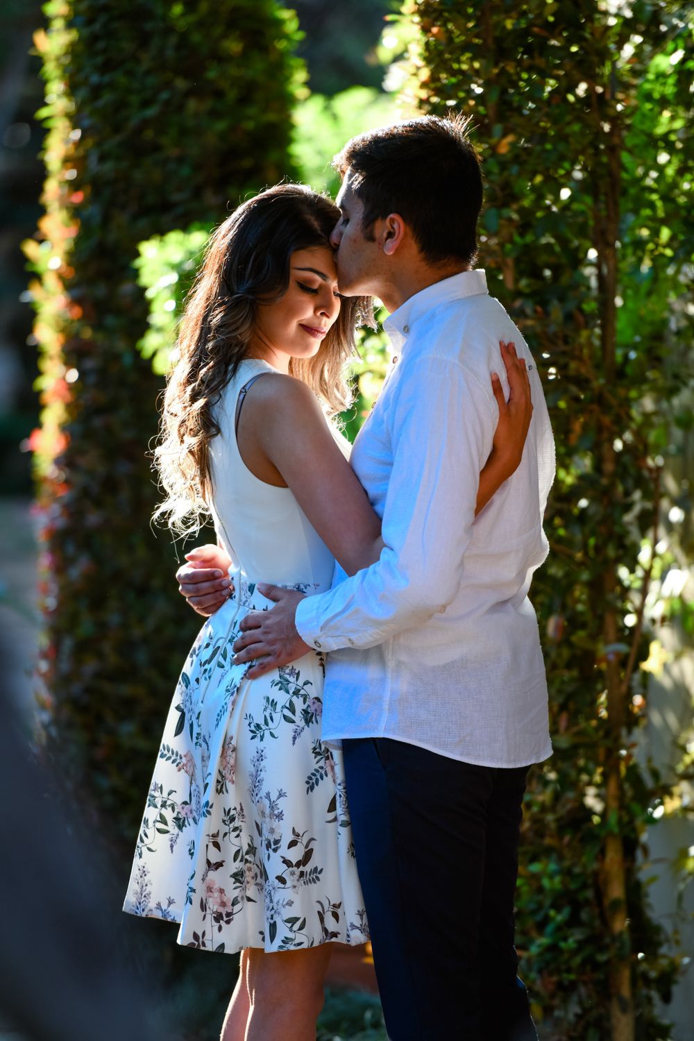 Sunlit portrait of a couple embracing against a wall covered in green ivy.