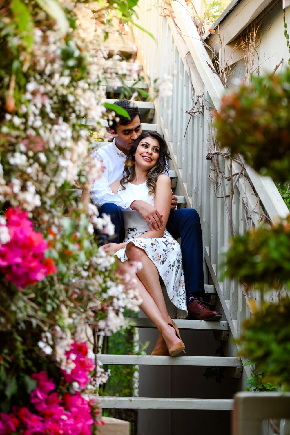 Couple sitting together on garden steps lined with potted plants and greenery.