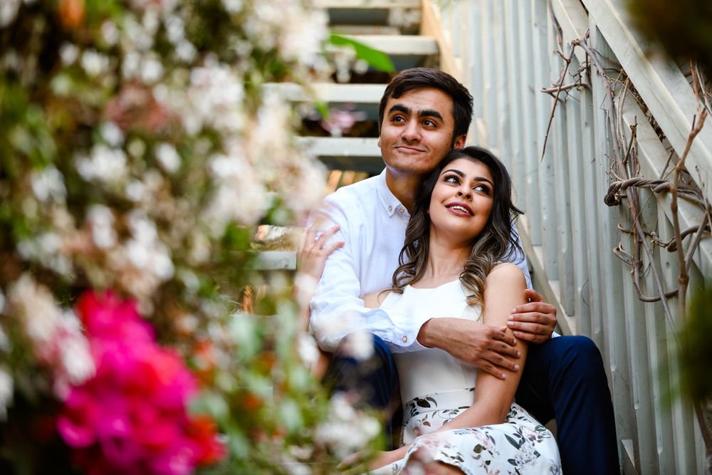 Couple sitting on stone stairs framed by bright pink bougainvillea flowers.