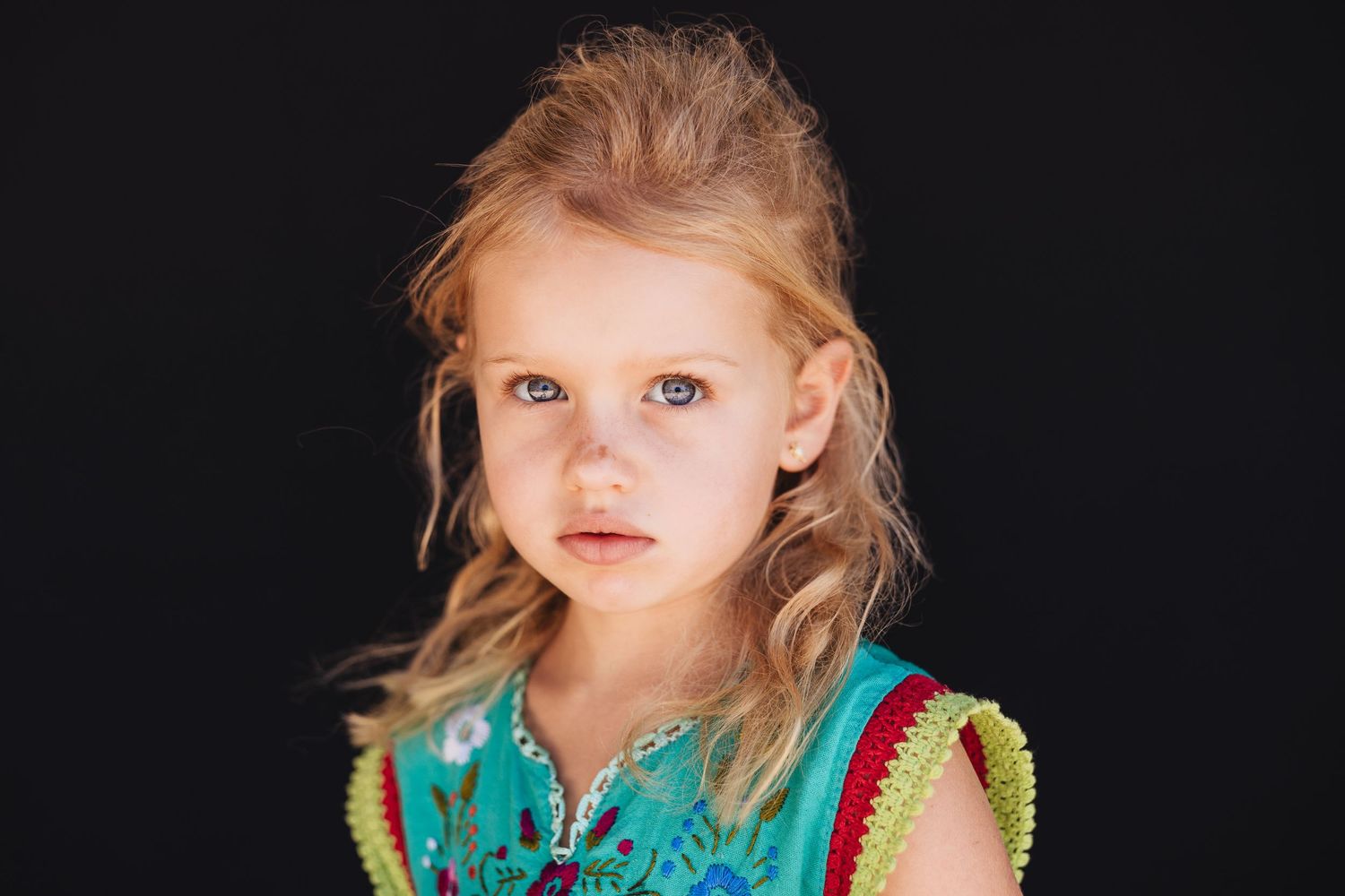 Portrait series of a young child in bright turquoise and yellow outfit against dark background.