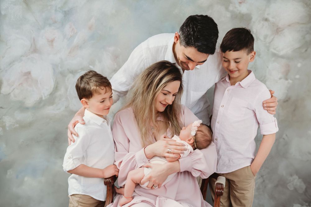 Family with three children gather around their newborn baby in coordinated casual outfits. Bellevue studio, WA
