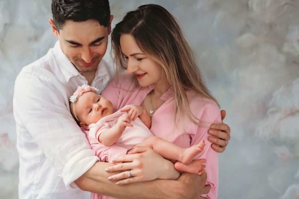 Parents share a tender moment with their newborn baby while wearing coordinated white and pink outfits. Bellevue studio, WA