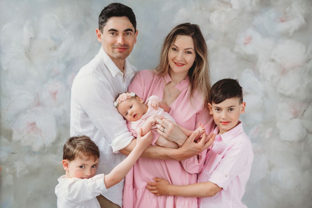Professional studio photo of family of five in matching white and pink outfits against painted backdrop. Bellevue studio, WA