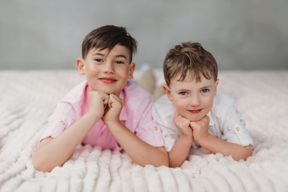 Two young children in pink and white outfits lie on white blanket with playful expressions. Bellevue studio, WA