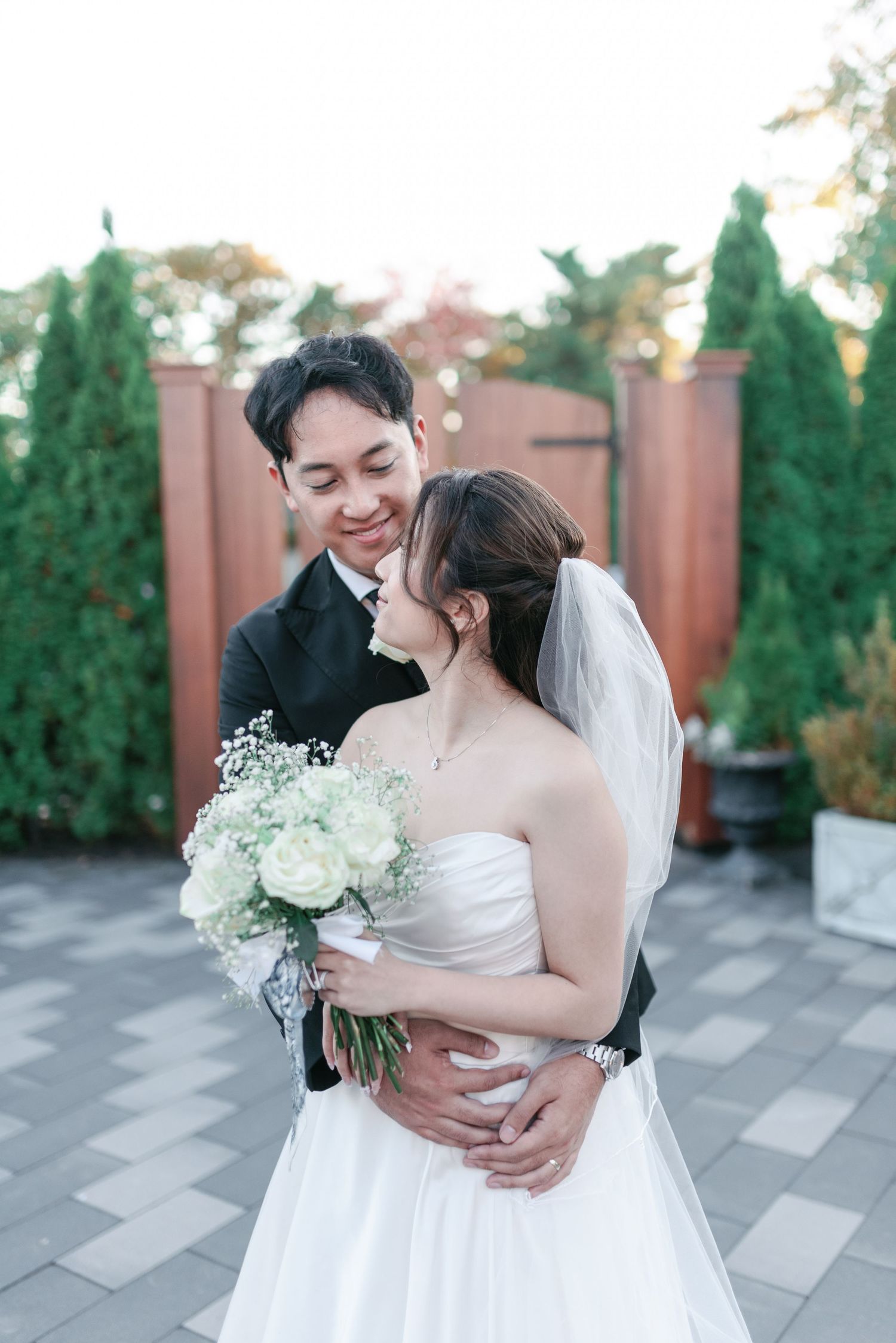 A tender wedding moment with white bouquet against evergreen garden backdrop.