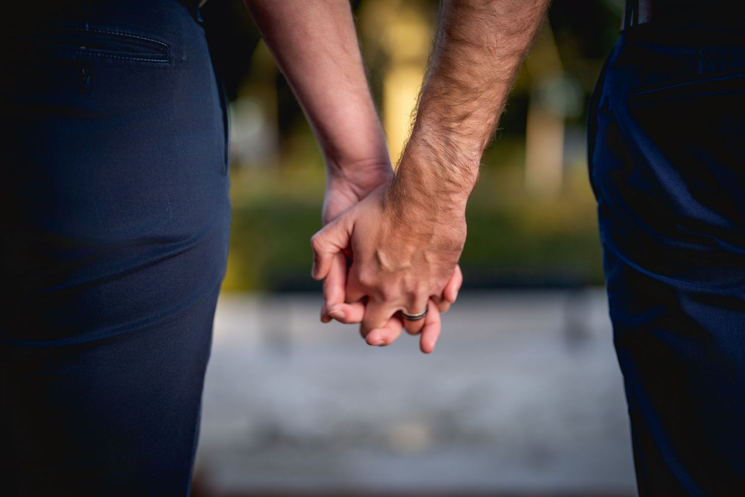 Close up view of two people holding hands together outdoors with blurred natural background.