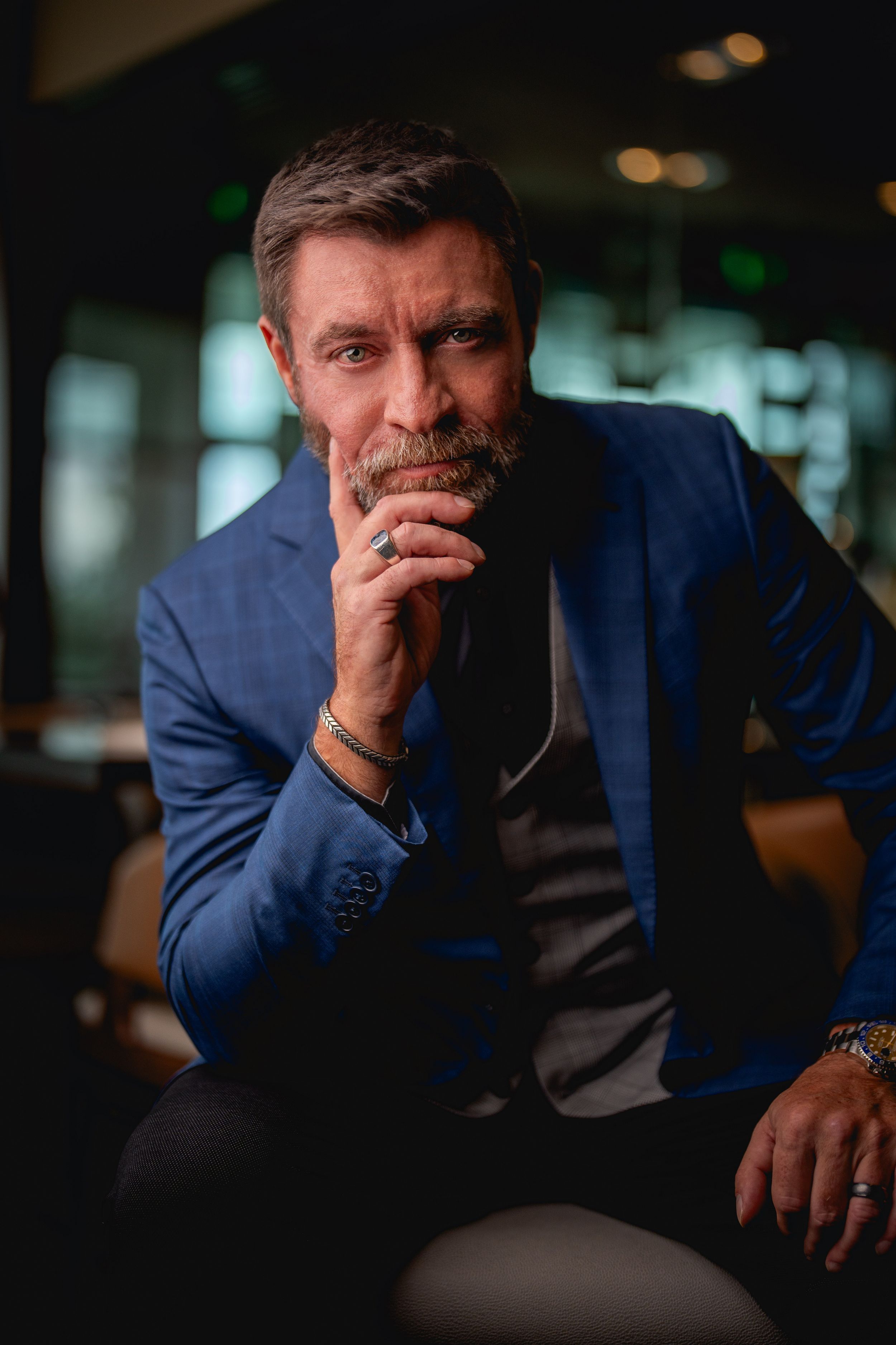 Professional in navy suit jacket sits thoughtfully in dimly lit environment.
