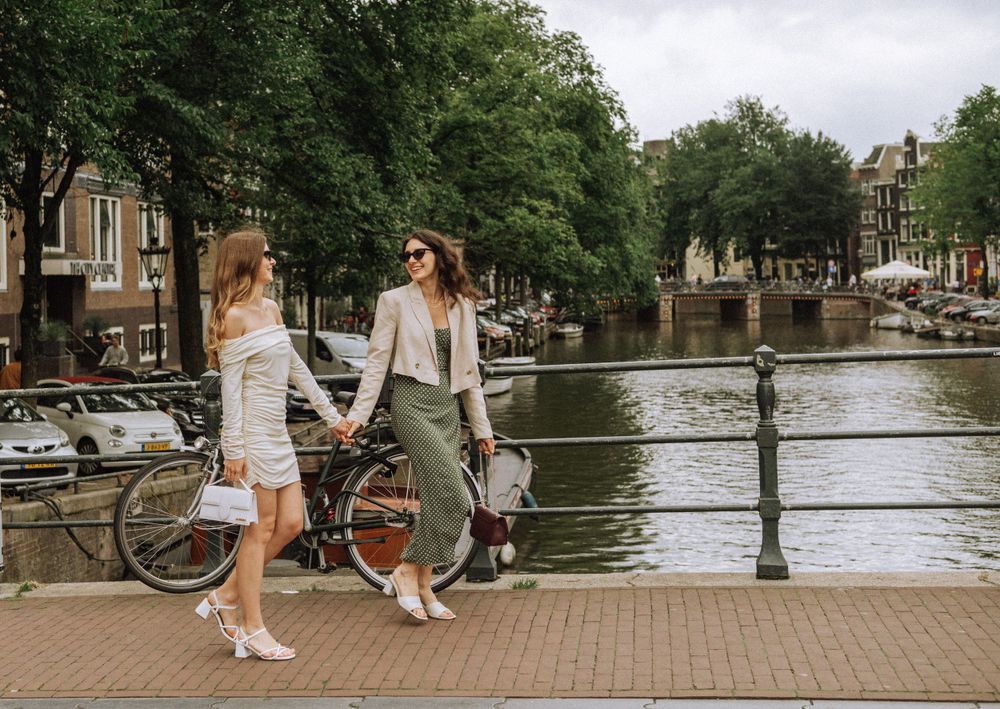 People relaxing along Amsterdam canal with historic buildings and bicycles visible.